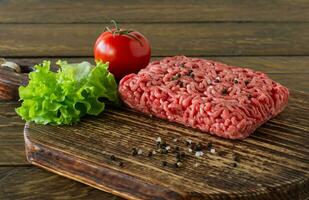 rå mald nötkött kött på en trä- skärande styrelse med grönsaker och kryddor. matlagning och friska äter begrepp. foto