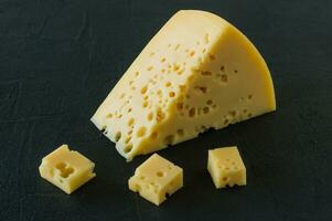 radamer ost på en svart betong bakgrund. triangel- bit av gul ko mjölk swiss ost med hål foto