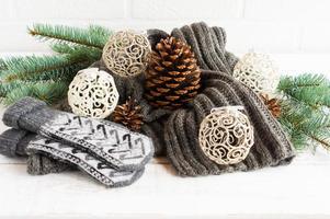 stickat värma scarf och vantar i de sammansättning med genombrutna bollar, koner och grenar av gran på en vit bakgrund. de begrepp mysigt jul. foto