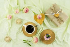romantisk skön sammansättning för hjärtans dag. en kopp av kaffe, en muffin med frukt och grädde, ljus, rosenknoppar. en gåva på en pastell bakgrund. foto