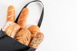 ett sortiment av bakad bröd i en svart bomull väska på en vit bakgrund. organisk bröd begrepp eko-shopping. topp se. foto