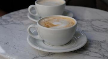 två koppar av cappuccino eller latte dekorerad med skum på marmor tabell bakgrund i kaffe affär. morgon- kaffe för par i kärlek. topp se. två vit muggar av kaffe. foto