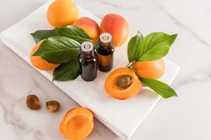 två medicinsk flaskor med naturlig aprikos grundläggande olja på en vit trä- podium med frukt. de begrepp av föryngring, avgörande och avslappning. foto