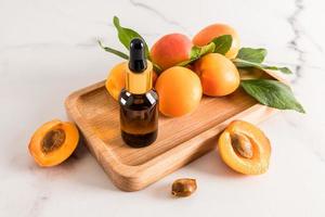 de perfekt ansiktsbehandling hud vård produkt. aprikos kärna olja i en kosmetisk flaska med en pipett på en trä- bricka och en marmor bakgrund. foto