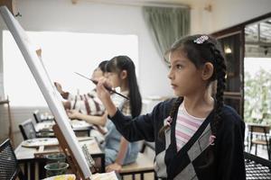 en liten flicka koncentrat på akryl Färg bild målning på duk med raser barn i ett konst klassrum, kreativ inlärning med talanger och Kompetens i de elementärt skola studio utbildning. foto