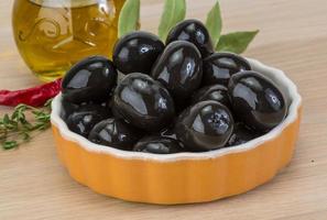 svart oliver i en skål på trä- bakgrund foto