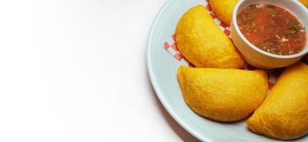 typisk colombianska empanadas med kryddad sås på vit bakgrund. foto