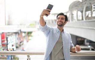 de ung man selfie med han själv förbi de använder sig av smartphone för ta Foto, och vänta för hans vän. foto