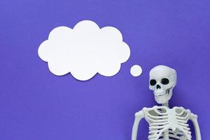 skelett på violett bakgrund med vit tom papper moln trodde bubbla. anatomisk plast modell mänsklig skelett med drömma text ballong. tömma tror moln, mockup, kopia Plats. lila halloween. foto