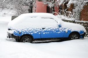 Foto av en bil täckt i en tjock lager av snö. konsekvenser av tung snöfall