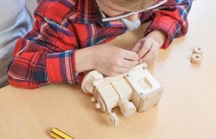 Lycklig fars dag och barndom begrepp. närbild av en far och en pojke son i glasögon arbete med hand verktyg, använder sig av en skruvmejsel, montering en trä- hus konstruktör på de tabell. foto