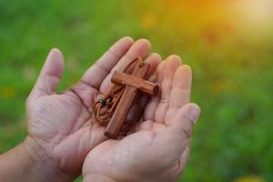 trä- korsa innehav i händer, begrepp för hoppas, kärlek, förlåtelse och tro i Jesus runt om de värld. mjuk och selektiv fokus, naturlig bokeh träd bakgrund. foto