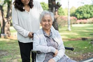 vårdgivare hjälp och vård asiatisk senior eller äldre gammal dam kvinna patienten sitter och glad på rullstol i parken, hälsosam stark medicinsk koncept. foto