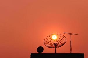 många typ av TV mottagare - TV antenn, satellit TV maträtt på de taket av byggnad med solnedgång himmel bakgrund i kväll, silhuett TV mottagare Utrustning på de byggnad. foto