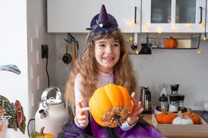 barn dekorerar de kök i Hem för halloween. flicka i en häxa kostym spelar med de dekor för de Semester - fladdermöss, domkraft lykta, pumpor. höst bekvämlighet i hus, scandi-stil kök, loft foto