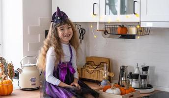 barn dekorerar de kök i Hem för halloween. flicka i en häxa kostym spelar med de dekor för de Semester - fladdermöss, domkraft lykta, pumpor. höst bekvämlighet i hus, scandi-stil kök, loft foto