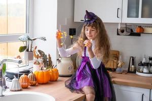 barn dekorerar de kök i Hem för halloween. flicka i en häxa kostym spelar med de dekor för de Semester - fladdermöss, domkraft lykta, pumpor. höst bekvämlighet i hus, scandi-stil kök, loft foto