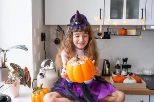 barn dekorerar de kök i Hem för halloween. flicka i en häxa kostym spelar med de dekor för de Semester - fladdermöss, domkraft lykta, pumpor. höst bekvämlighet i hus, scandi-stil kök, loft foto