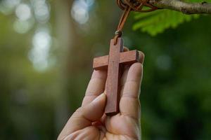 trä- korsa innehav i händer, begrepp för hoppas, kärlek, förlåtelse och tro i Jesus runt om de värld. mjuk och selektiv fokus, naturlig bokeh träd bakgrund. foto