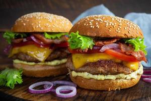 utsökt nötkött hamburgare med bacon skiva, ost, sallad och tomat. gott snabbmat burger foto