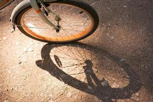 cykel hjul rider längs ett asfalt väg och kastar skugga, på solig sommar dag foto