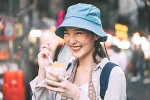 ung vuxen asiatisk foodie kvinna ryggsäcksresenär äter asiatisk efterrätt på Chinatown street food. foto