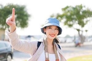 gående ung vuxen sydöst asiatisk kvinna resande ha på sig blå hatt och ryggsäck under solljus foto
