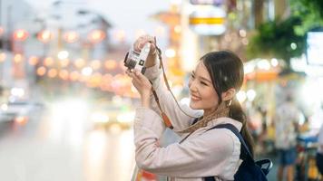 ung vuxen asiatisk kvinna resande använder sig av kamera för Foto på natt stad med bokeh.