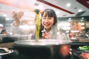 Lycklig ung asiatisk kvinna japansk thai studerande äter shabu shabu japan sukiyaki restaurang. foto