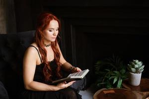 rödhårig kvinna i en stol läsning en bok foto