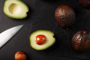 skivad och hela organisk avokado hass med en kniv på en svart bakgrund. foto