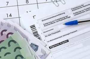tysk beskatta form med penna och europeisk pengar räkningar lögner på kontor kalender. skattebetalarna i Tyskland använder sig av euro valuta till betala skatter foto