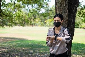 selektiv fokus på ansikte av ung skön asiatisk kvinnor bär kirurgisk ansikte mask använder sig av smart Kolla på till Spår aktivitet innan övning eller löpning på de parkera i de morgon. ny vanligt livsstil. foto