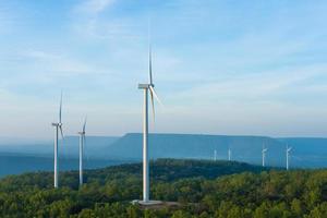 landskap Sol uppsättning skott av vind turbiner bruka på de grön gräs fält med klar blå himmel och berg på de bakgrund. alternativ grön energi som generera elektricitet från naturlig vind kraft. foto