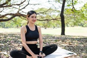 selektiv fokus på ansikte av ung skön asiatisk kvinnor leende medan värma upp innan övning yoga med naturlig och träd på bakgrund. friska livsstil för Bra kropp och hälsa skick. foto