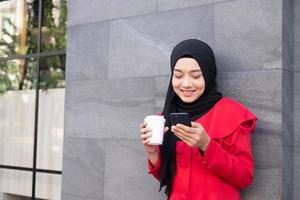 skön öst asiatisk islamic kvinnor bär hijab med formell klänning. innehav kaffe kopp och gående i urban stad område, känsla Lycklig och leende. människor livsstil begrepp med kopia Plats. foto