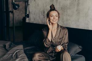 ung vacker europeisk kvinna i sidenpyjamas tar hand om sin hud och kropp foto