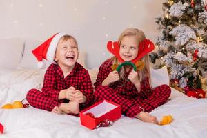 två Lycklig barn i pyjamas för jul är sortering presenterar och spelar med jul leksaker. hög kvalitet Foto