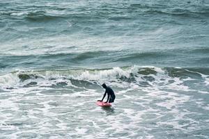 manlig surfare i baddräkt i havets vågor med röd surfbräda foto