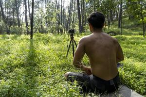 ung man praktiserande yoga asana, balans, mediterar medan stående på ett ben på sporter matta på grön gräs i parkera. använder sig av läsplatta för uppkopplad klass. foto