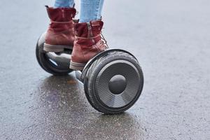 stänga upp av kvinna använder sig av hoverboard på asfalt väg. fötter på elektrisk skoter utomhus- foto