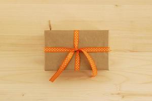 gåva låda insvept av hantverk papper och orange band på de trä- bakgrund, topp se. foto