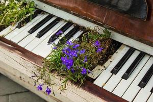 de gammal vit piano med lila blommor på de gata. foto