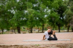 liten söt asiatisk flicka praktiserande yoga utgör på en matta i parkera, friska och övning begrepp foto