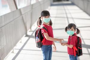 liten flicka och syster bär ansikte mask gående till skola under coronavirus utbrott. säkerhet mask för sjukdom förebyggande. mamma och unge på skola under covid 19 pandemier. foto