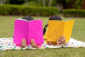 två skön liten flickor läsning böcker i de trädgård , Sammanträde på gräs. de begrepp av utbildning och vänskap. foto