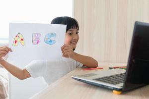 asiatisk flicka studerande uppkopplad inlärning klass studie uppkopplad med bärbar dator på Hem. foto