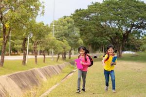 tillbaka till skola. två söt asiatisk barn flickor med skola väska innehav bok och promenad tillsammans i de skola foto