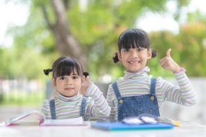 två studerande liten asiatisk flickor läsning de bok på tabell foto
