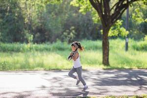 Lycklig barn flicka löpning i de parkera i sommar i natur. värma solljus blossa. asiatisk liten är löpning i en parkera. utomhus- sporter och kondition, övning och konkurrens inlärning för unge utveckling. foto